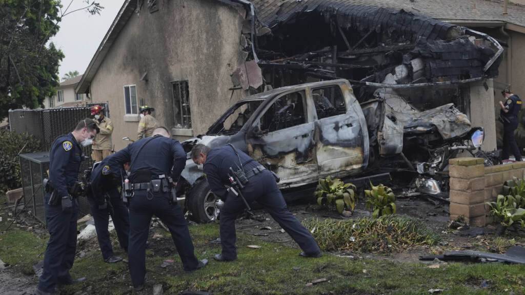 Polizisten ermitteln an der Stelle, an der ein Kleinflugzeug in einen Stadtteil von San Diego gestürzt ist, wobei mehrere Häuser in Brand gerieten und mehrere Häuserblocks evakuiert werden mussten. Foto: Gregory Bull/AP/dpa