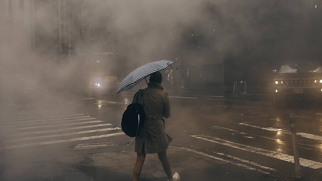 Ein Person geht im Regen über eine Straße. Heftiger Regen hat in der Millionenmetropole New York zu Überschwemmungen und Sperrungen von Autobahnen, Straßen und Flughafenterminals geführt. Foto: Andres Kudacki/AP/dpa
