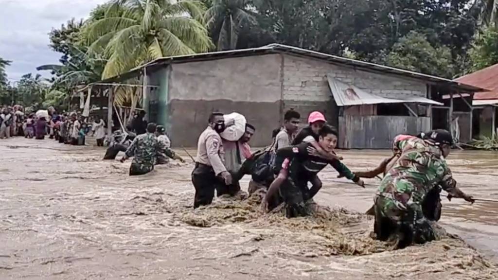 Soldaten und Polizisten helfen Anwohnern über eine überflutete Straße. Foto: Uncredited/AP/dpa