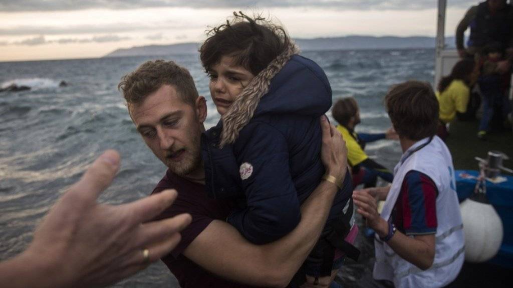 Ein Fotograf hilft auf der griechischen Insel Lesbos einem Mädchen an Land, nach dem es zusammen mit über 100 anderen Flüchtlingen in einem Boot von der türkischen Küste über das Mittelmeer gekommen war (Archiv)