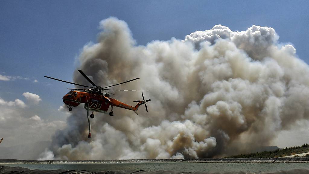 Ein Löschhubschrauber fliegt während eines Waldbrandes über einen Wasserspeichertank. Foto: Valerie Gache/AP/dpa