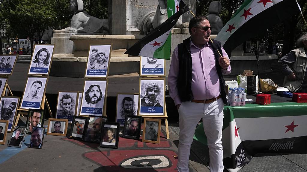 Aktivisten halten syrische Flaggen neben Porträts von mutmaßlichen Opfern des syrischen Regimes während einer Demonstration vor einem Gerichtssaal in Paris. Dort hat der Prozess gegen drei ranghohe syrische Beamte begonnen, die für den Tod von zwei französischen Staatsbürgern in Syrien verantwortlich sein sollen. Foto: Michel Euler/AP/dpa