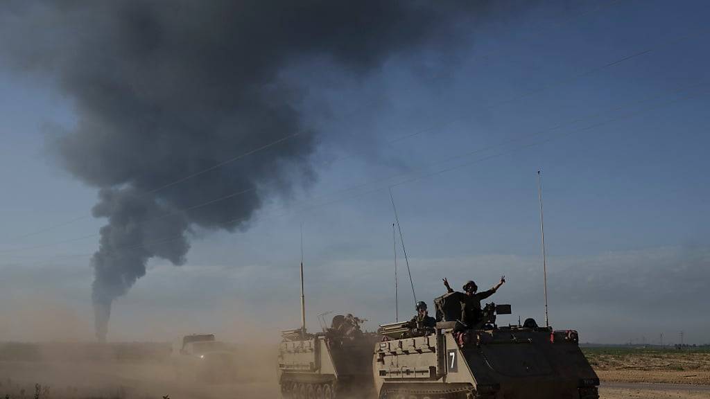 Israelische Soldaten auf gepanzerten Mannschaftstransportern (APC) der Armee nahe der Grenze zwischen Israel und Gaza, während im Gazastreifen Rauch in den Himmel steigt, vom Süden Israels aus gesehen. Foto: Leo Correa/AP/dpa