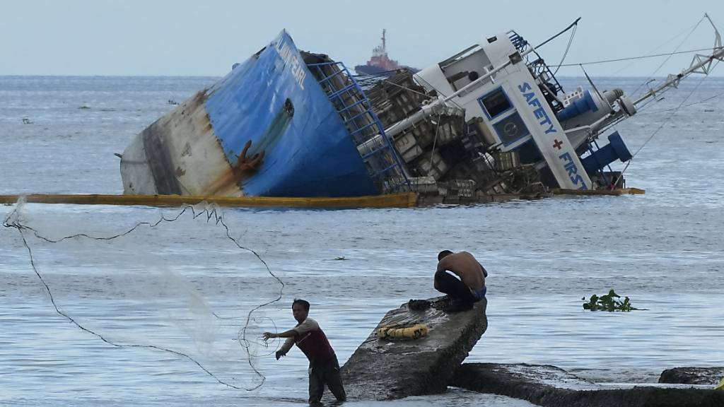 Ein Fischer wirft sein Netz neben der halb gesunkenen Frachtschiff MV Palawan Pearl aus. Nach einer Schiffskollision vor der Küste der Philippinen befürchten die Behörden eine mögliche Ölkatastrophe. Foto: Aaron Favila/AP/dpa