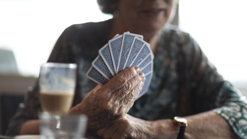 Private Vorsorge: Ältere Frau hält aufgefächerte Karten in der Hand. Im Vordergrund ein Kafi im Glas.