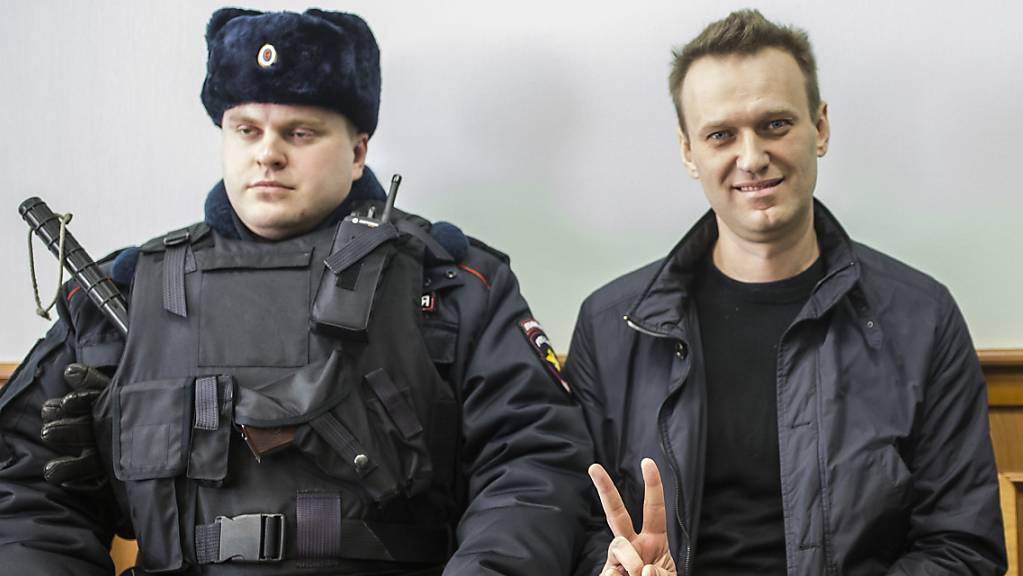 Alexej Nawalny (r) zeigt ein Victory-Zeichen, während er neben einem Sicherheitsbeamten im Gericht sitzt. . Foto: Evgeny Feldman/AP/dpa