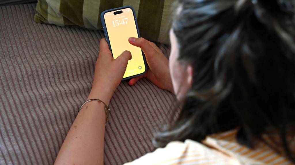 SYMBOLBILD - Eine Jugendliche liegt auf einem Sofa und entsperrt ihr Smartphone. Foto: Elisa Schu/dpa