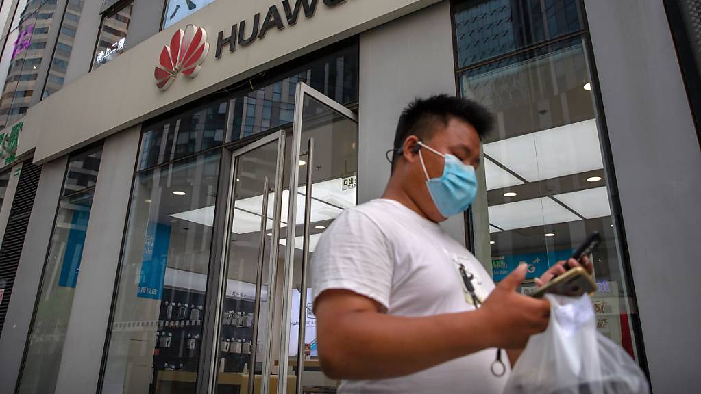 ARCHIV - Ein Mann mit Gesichtsmaske schaut auf sein Smartphone, als er an einem Huawei-Laden in Peking vorbeigeht. Der chinesische Technologiekonzern Huawei soll nun endgültig nicht am Ausbau des superschnellen 5G-Mobilfunknetzes in Großbritannien beteiligt werden. Foto: Mark Schiefelbein/AP/dpa