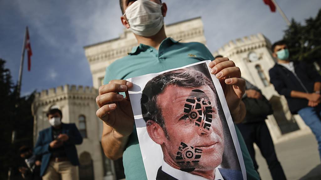 Ein junger Mann hält in Istanbul ein mit einem Schuhabdruck versehenes Foto von Emmanuel Macron in die Kamera. Foto: Emrah Gurel/AP/dpa
