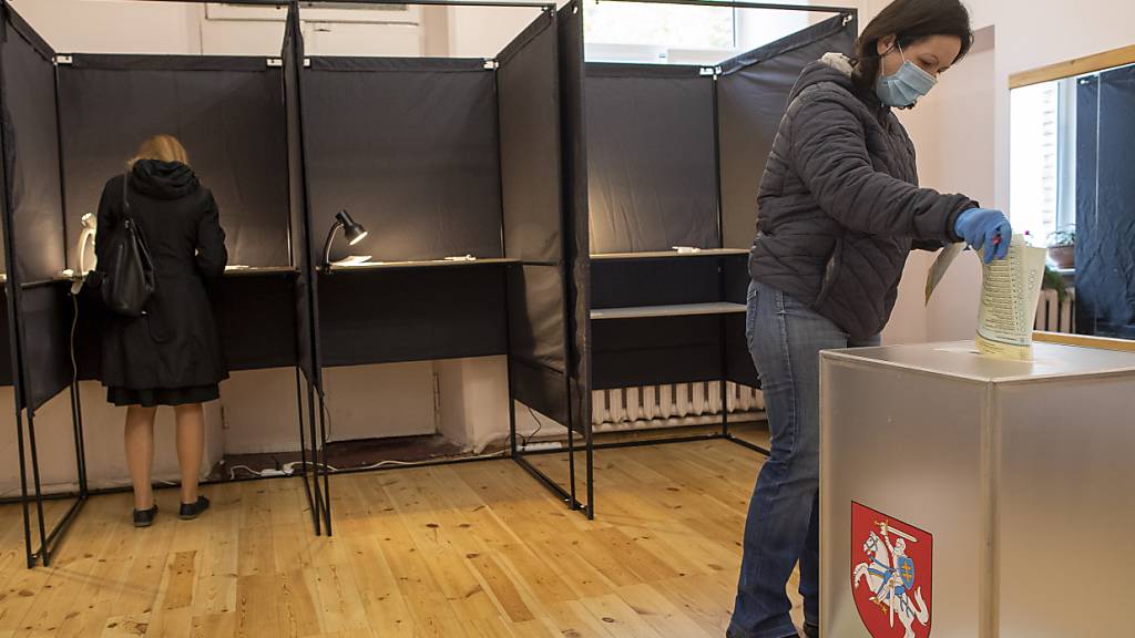Eine Frau trägt einen Mund-Nasen-Schutz, während sie ihren Stimmzettel in eine Wahlurne wirft. Die Bürger in Litauen sind dazu aufgerufen, die 141 Sitze im Parlament zu erneuern. Foto: Mindaugas Kulbis/AP/dpa