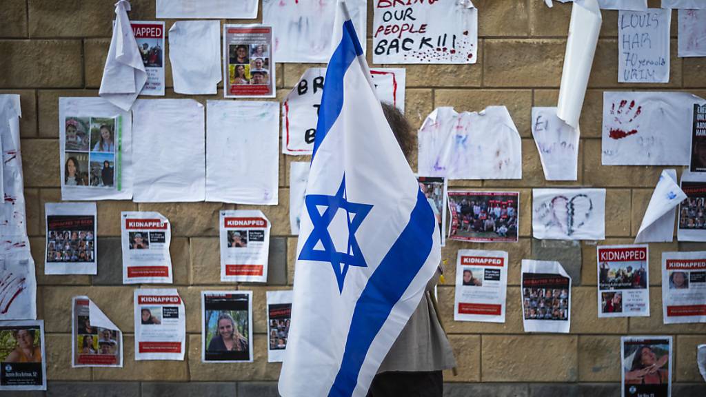 Eine Frau, die eine israelische Fahne hält, guckt sich Plakate an, auf denen Personen zu sehen sind, die von der Hamas entführt wurden. Foto: Ilia Yefimovich/dpa