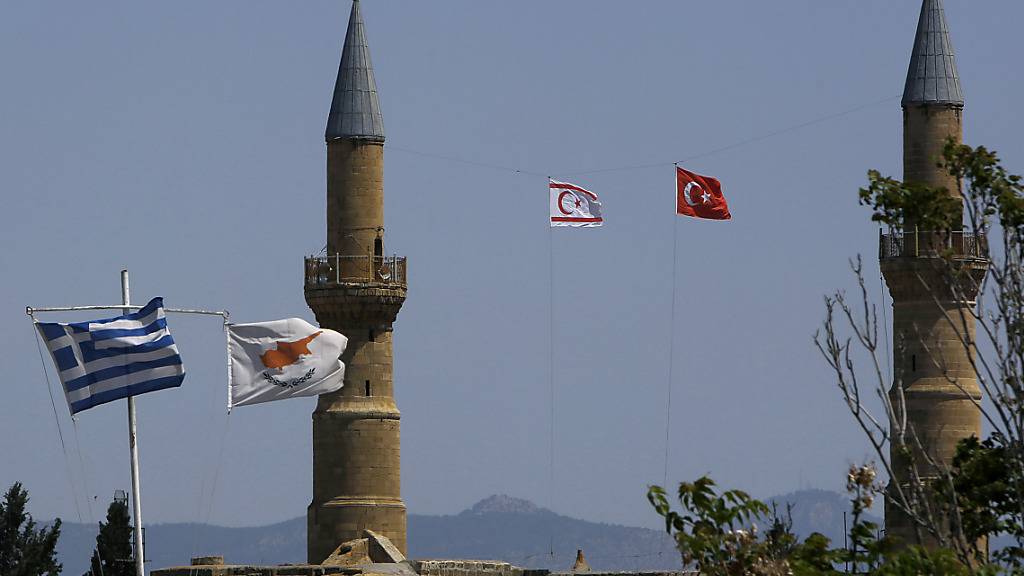 Griechische und zypriotische Flaggen flattern im Wind im südlichen Teil. Währenddessen im Norden, im türkisch besetzten Gebiet, eine türkische und eine türkisch-zypriotische Flagge auf einem Minarett der Selimiye-Moschee in der geteilten Hauptstadt Zyperns wehen. Foto: Petros Karadjias/AP/dpa