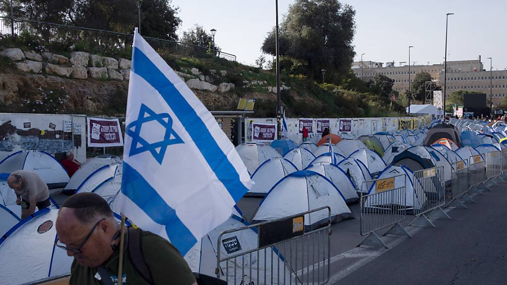 Mit einer israelischen Flagge in der Hand geht ein Mann an einem von Regierungsgegnern errichtetem Zeltlager in der Nähe der Knesset, dem israelischen Parlament, vorbei. Foto: Leo Correa/AP