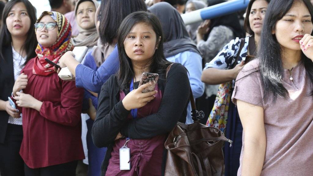Warten auf Informationen: Menschen im Freien warten in Jakarta auf die Rückkehr in die Gebäude.