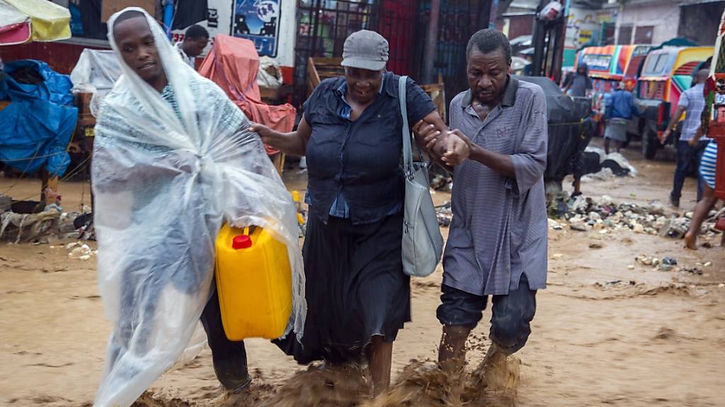dpatopbilder - Menschen gehen während des Tropensturms «Laura» über eine überschwemmte Straße in Haitis Hauptstadt Port-au-Prince. Foto: Dieu Nalio Chery/AP/dpa