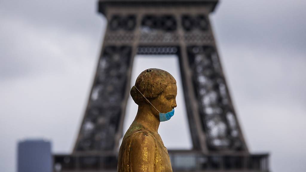 Eine goldene Statue am Pariser Platz Trocadéro trägt eine Schutzmaske. Im Hintergrund ist das berühmte Wahrzeichen Eiffelturm zu sehen. (Archivbild)
