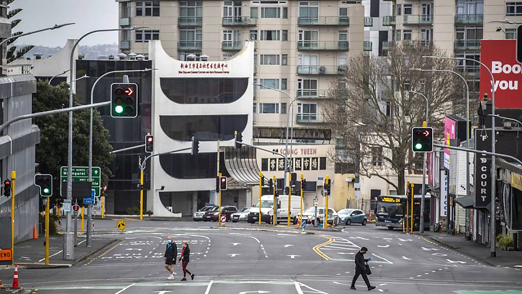 Menschen überqueren eine fast leere Straße im zentralen Geschäftsviertel von Auckland. Die Regierung von Ministerpräsidentin Jacinda Ardern gab am Montag bekannt, dass die neuseeländische Metropole eine weitere Woche im strikten Corona-Lockdown bleibt.