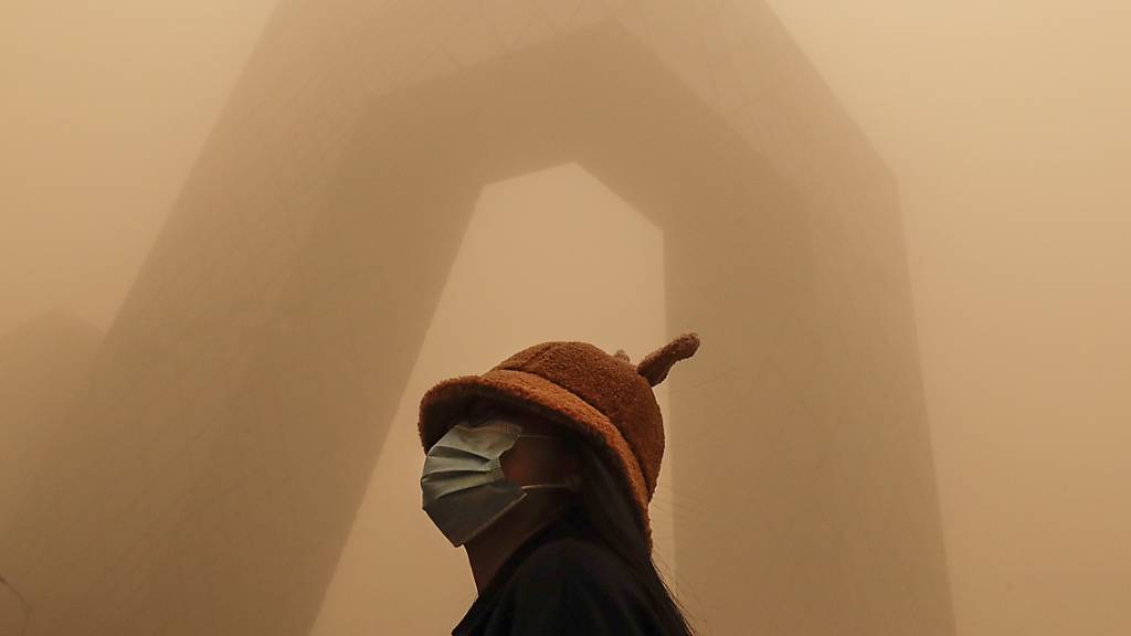 Eine Frau, die eine Gesichtsmaske trägt, steht vor dem Gebäude des China Central Television (CCTV), während die Hauptstadt von einem Sandsturm getroffen ist. Der Sandsturm hat den Himmel über Peking vernebelt und die Luftqualität ist schlecht.