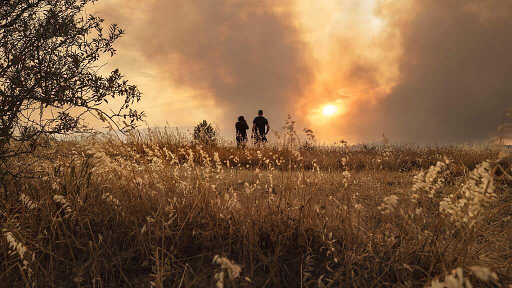 Menschen beobachten einen Waldbrand in Südfrankreich. Im Kampf gegen den Brand zwischen den Städten Narbonne und Carcassonne sind über 1000 Feuerwehrleute und Retter im Einsatz. Foto: Idriss Bigou-Gilles/AFP/dpa