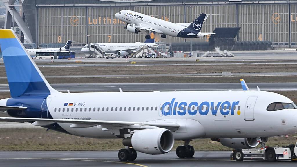 ARCHIV - 14.02.2024, Hessen, Frankfurt/Main: Während eine Maschine der Lufthansa startet, wird ein Passagierflugzeug der Discover Airlines am Frankfurter Flughafen von einem Schlepper gezogen. (zu dpa: «Urabstimmung über Streik bei Lufthansa-Tochter endet») Foto: Arne Dedert/dpa +++ dpa-Bildfunk +++ (KEYSTONE/DPA/Arne Dedert)