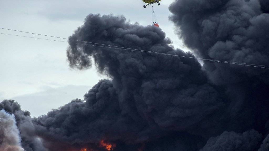 Ein Helikopter versucht das Feuer einzudämmen. Die brennenden Autoreifen verursachen eine Giftwolke.