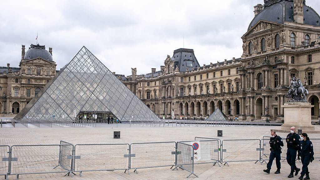 ARCHIV - Der Louvre ist geschlossen, der Platz davor ist leer. Nur drei Polizisten gehen an einer Absperrung entlang. Foto: Elko Hirsch/dpa