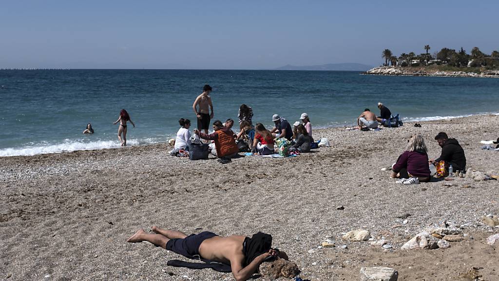 Menschen genießen einen sonnigen Tag an einem Strand im Athener Vorort Glyfada. Foto: Yorgos Karahalis/AP/dpa