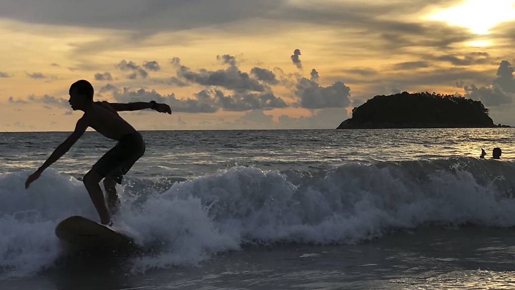 Ein Surfer nimmt vor dem Strand Kata Beach eine Welle bei Sonnenaufgang. Thailand plant, geimpften Ausländern zu erlauben, die südliche Ferieninsel Phuket ohne Quarantäne bei der Ankunft zu besuchen, zur Wiederbelebung der durch die Corona-Pandemie angeschlagene Tourismusindustrie. Foto: Adam Schreck/AP/dpa