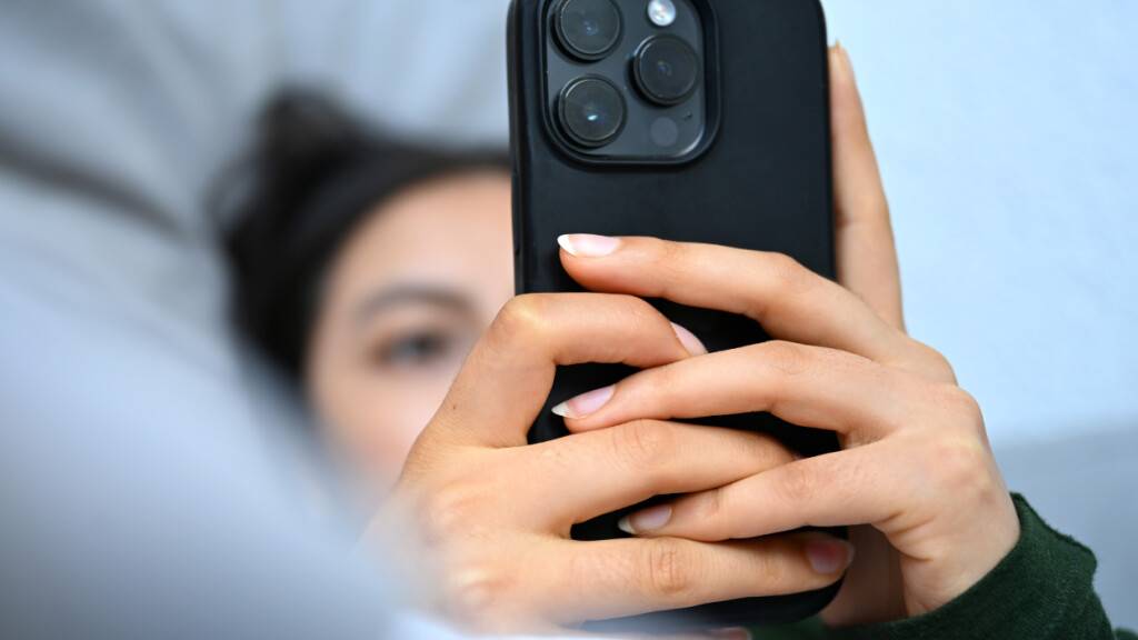 Eine junge Frau liegt mit ihrem Handy auf der Couch und blickt auf das Display.
