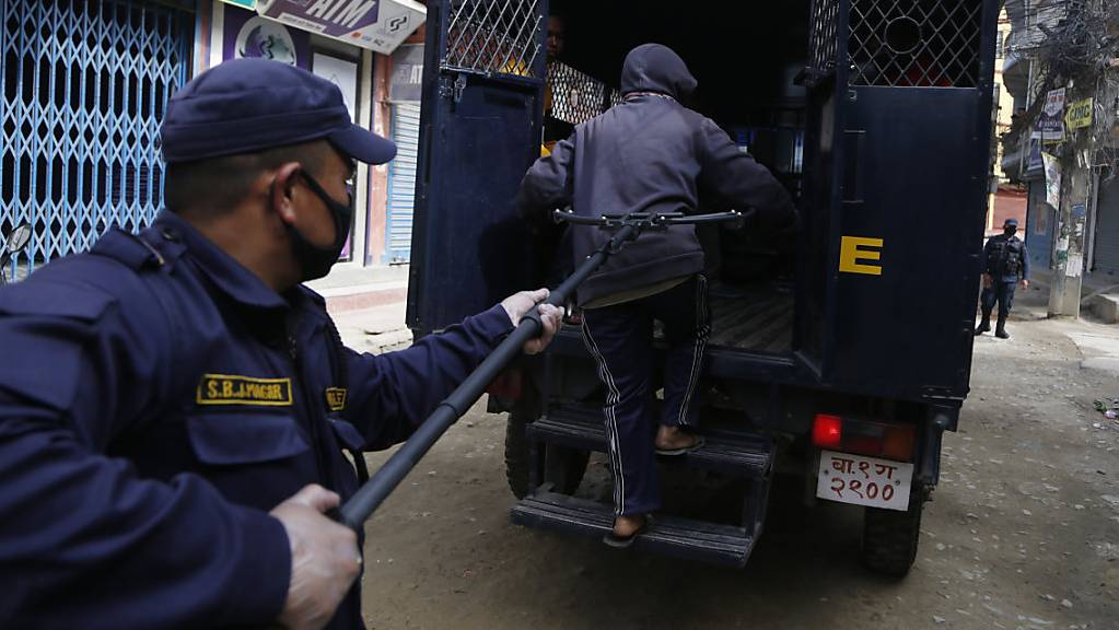 Ein Polizist in Nepal nimmt eine Person fest, die gegen die Ausgangssperre verstossen hat. Wegen der Corona-Pandemie benutzt die Polizei in Nepal lange Klammern.