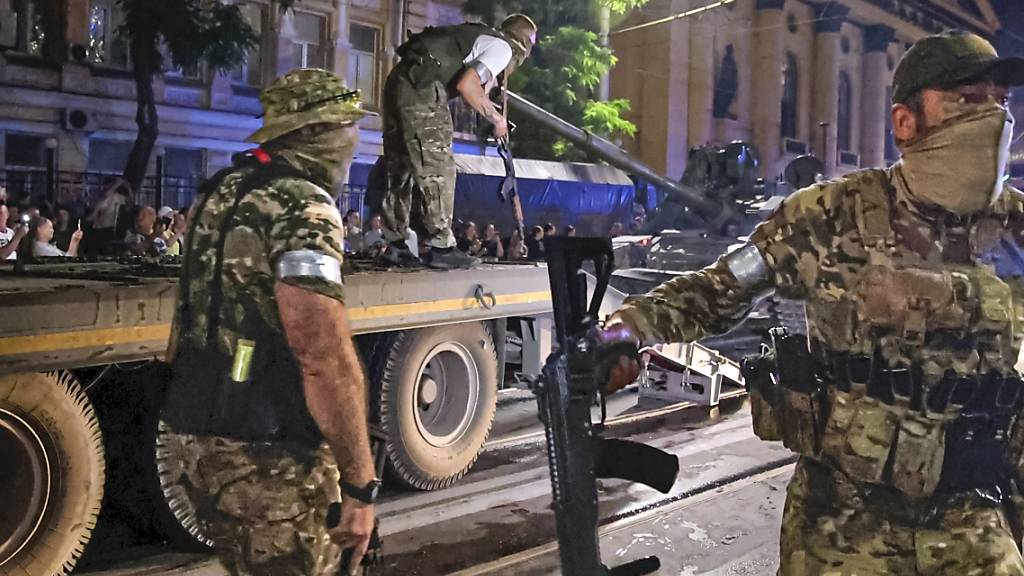 ARCHIV - Mitglieder der Söldnergruppe Wagner bewachen einen Bereich, während andere ihren Panzer auf einen Lastwagen auf einer Straße in Rostow am Don laden. Gut anderthalb Jahre nach Beginn des russischen Angriffskriegs gegen die Ukraine will Großbritannien die russische Privatarmee Wagner zu einer terroristischen Organisation erklären lassen. Foto: Vasily Deryugin/Kommersant Publishing House/AP/dpa