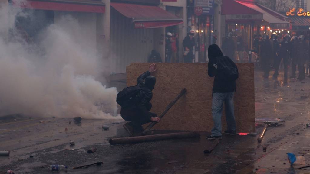 Demonstranten schützen sich hinter einer Holzplatte gegen Tränengas- und Gummigeschosse. Foto: Marcus Golejewski/dpa