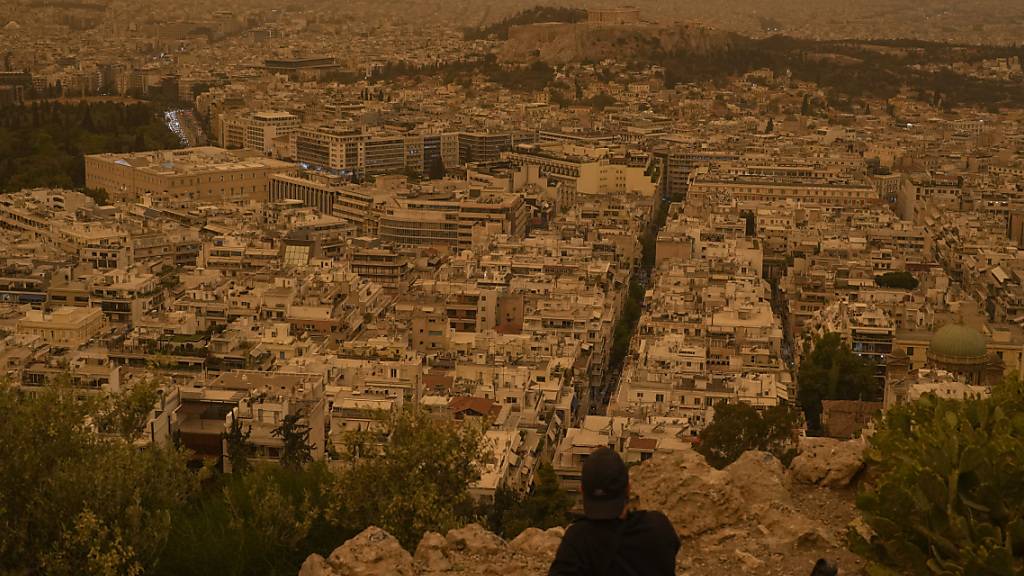 dpatopbilder - Ein Tourist sitzt auf einer Bank auf dem Lycabettus-Hügel in Athen. Saharastaub hat den Himmel über der griechischen Hauptstadt eingetrübt. Foto: Petros Giannakouris/AP/dpa