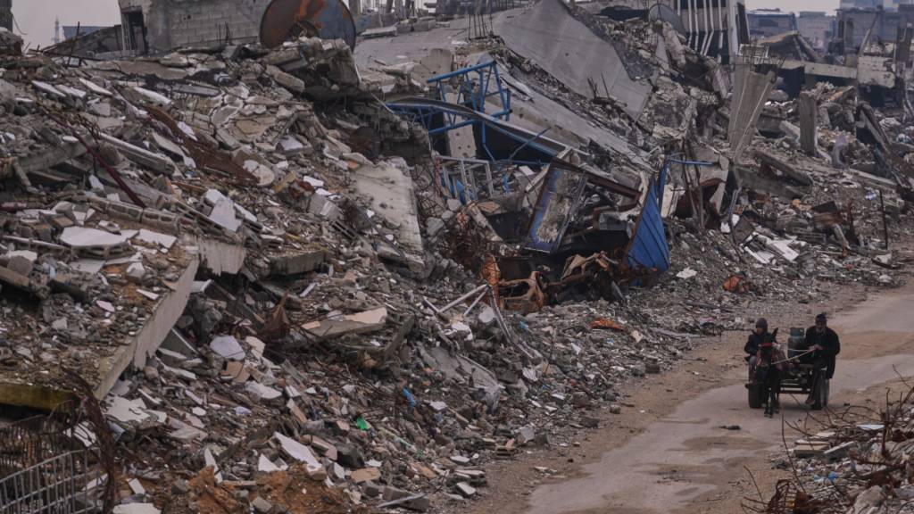 ARCHIV - Palästinenser gehen eine Straße in der Stadt Gaza entlang, die von Gebäuden umgeben ist, die bei israelischen Luft- und Bodenangriffen im Viertel Sheikh Radwan zerstört wurden. Foto: Abdel Kareem Hana/AP/dpa