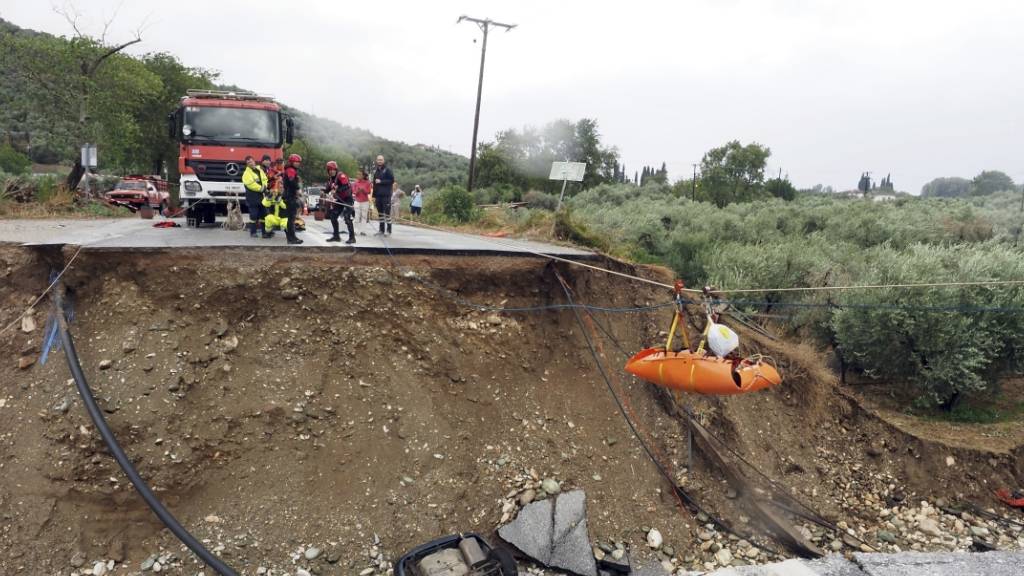 dpatopbilder - Feuerwehrleute heben im griechischen Kala Nera einen Nierenpatienten über eine durch einen Regensturm beschädigte Straße. Foto: Thodoris Nikolaou/AP/dpa
