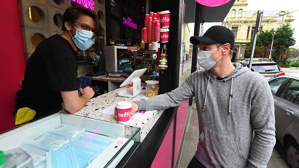 Barista Alex Pallas (left) serves a customer a coffee and facemask at Eeffoc Cafe in Prahran, Melbourne, Wednesday, July 22, 2020.  Eeffoc Cafe in Prahran is handing out single use face masks with takeaway coffee purchase. (AAP Image/James Ross) NO ARCHIVING
