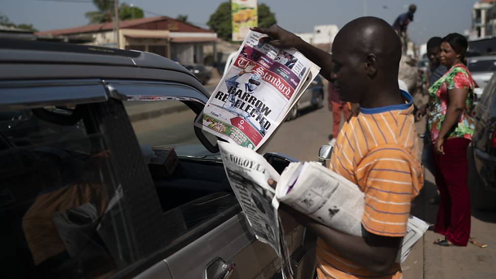 Ein Mann verkauft eine Zeitung, deren Titelseite die Wiederwahl des gambischen Präsidenten Barrow zeigt mit der Schlagzeile «Barrow re-elected». Foto: Leo Correa/AP/dpa