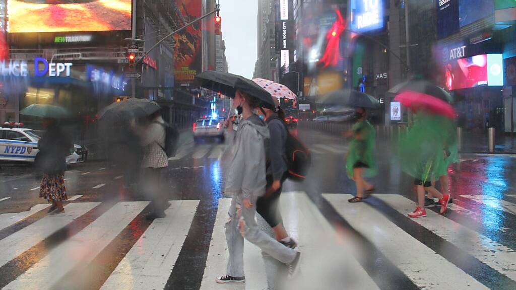 Fußgängerinnen und Fußgänger bei der Straßenüberquerung am Times Square schützen sich mit Regenschirmen vor starkem Regen. Der Tropensturm «Henri» hat in der U-Bahnstation Times Square - 42nd Street einen Wasserschaden verursacht. Foto: Niyi Fote/TheNEWS2 via ZUMA Press Wire/dpa