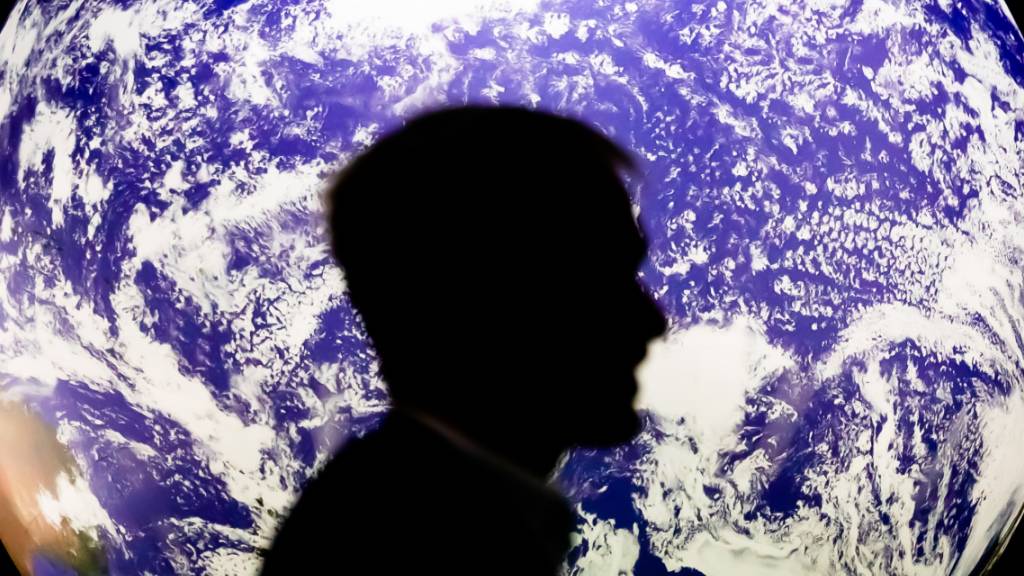 Ein Mann sitzt bei der UN-Klimakonferenz COP26 vor einem leuchtenden Globus. Foto: Christoph Soeder/dpa