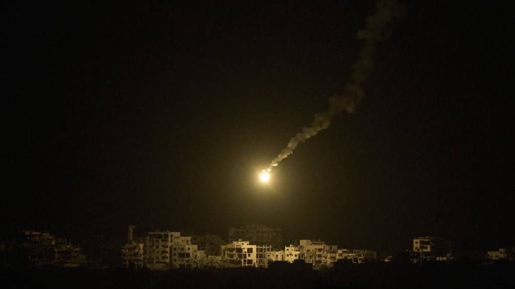dpatopbilder - Eine Leuchtrakete der israelischen Armee ist über Gebäuden zu sehen, die während der israelischen Boden- und Luftoperationen im nördlichen Gazastreifen zerstört wurden, gesehen vom Süden Israels aus. Foto: Leo Correa/AP/dpa