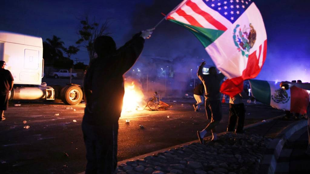 dpatopbilder - Ein Demonstrant schwenkt eine amerikanische und eine mexikanische Flagge während einer Demonstration in Compton, Kalifornien. Foto: Ethan Swope/AP/dpa