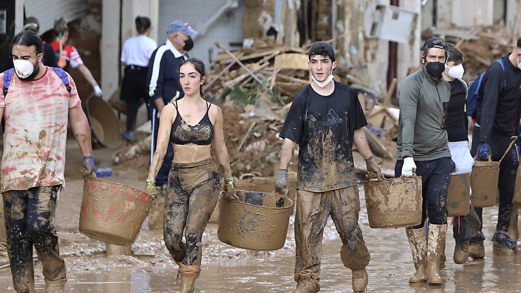 Freiwillige tragen Eimer mit Schlamm bei den Aufräumarbeiten in Paiporta bei Valencia in Spanien. Foto: Hugo Torres/AP/dpa