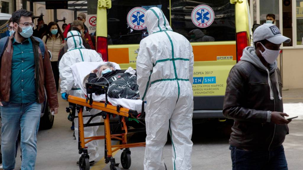 Medizinische Mitarbeiter in Schutzausrüstung transportieren einen Patienten auf einer Trage, um ihn in einem Krankenhaus in Athen zu verlegen. Foto: Marios Lolos/Xinhua/dpa
