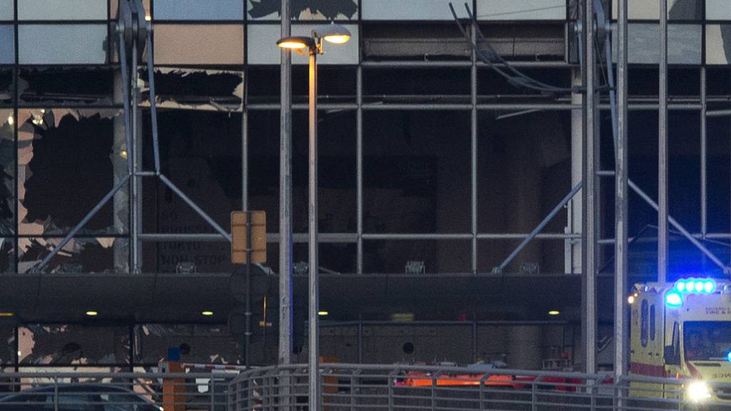 ARCHIV - Ein Krankenwagen fährt an der zerstörten Fassade des Terminals des Flughafens Zaventem, als er nach den beiden tödlichen Anschlägen den Ort verlässt. Im Prozess um die islamistischen Anschläge 2016 in Brüssel haben sich die Geschworenen und das Gericht zu Beratungen über die Strafen für die Terroristen zurückgezogen. Foto: Peter Dejong/AP/dpa