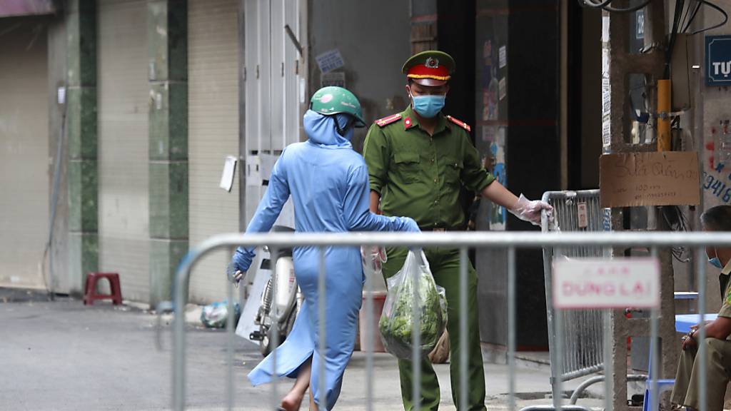 ARCHIV - Eine Frau geht vor einem Supermarkt in Hanoi an einem Polizisten mit Mundschutz vorbei. Foto: Hau Dinh/AP/dpa