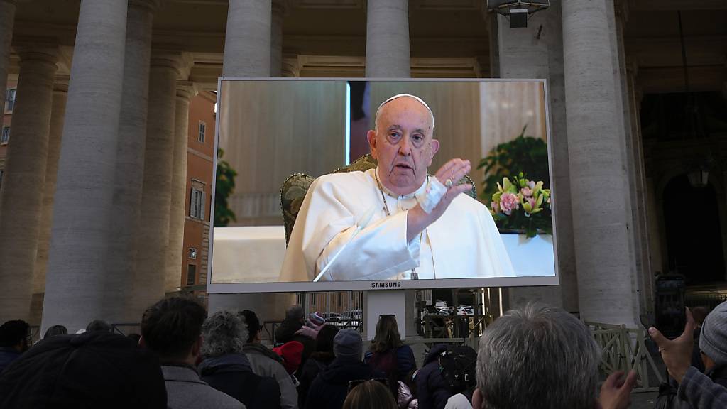 Papst Franziskus ist auf einem Monitor auf dem Petersplatz zu sehen, um die Gläubigen zu segnen, die sich auf dem Platz versammelt haben. Foto: Alessandra Tarantino/AP/dpa