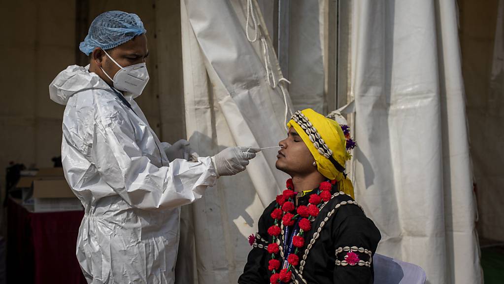 ARCHIV - Ein Mitarbeiter des Gesundheitswesen in Indien entnimmt einem Mann einen Abstrich für einen Corona-Test. Foto: Altaf Qadri/AP/dpa