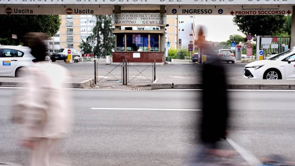 Passanten gehen am Haupteingang der Poliklinik «Agostino Gemelli» vorbei, in der Papst Leo XIV. in den nächsten Tagen zur Entfernung eines Lungenknotens stationär aufgenommen werden soll. Foto: Andrew Medichini/AP/dpa