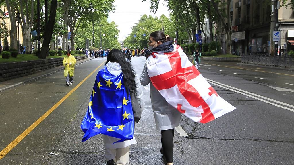Zwei Demonstranten mit georgischer National- und EU-Flagge gehen während eines Protestes der Opposition gegen das «russische Gesetz» im Zentrum von Tiflis auf das Parlamentsgebäude zu. Foto: Shakh Aivazov/AP/dpa