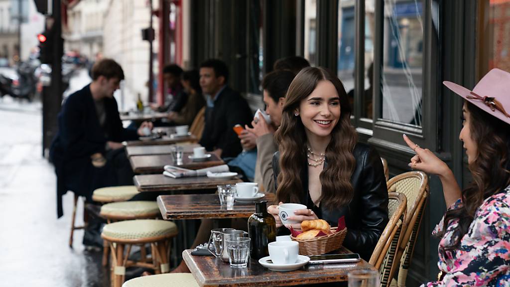 Emily (Lily Collins, Mitte) sitzt mit einer Freundin im Café – eine Filmszene aus der ersten Staffel der Netflix-Serie «Emily in Paris».